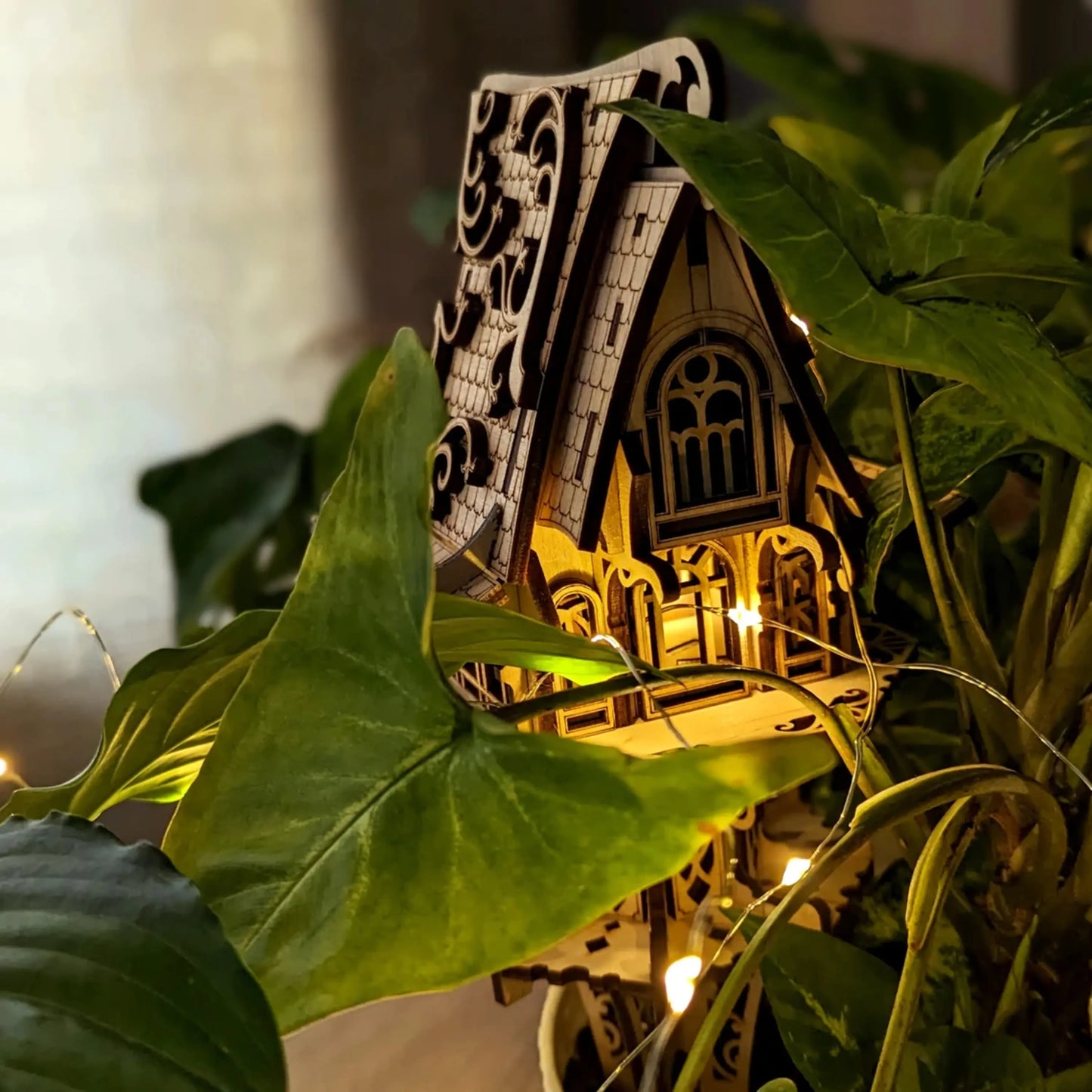Cozy night shot of a laser cut plywood elf house glowing from within using warm fairy lights inside green foliage.