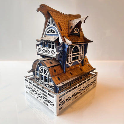 A laser cut plywood miniature gnome house nestled inside a white potted plant with green leaves and gravel.