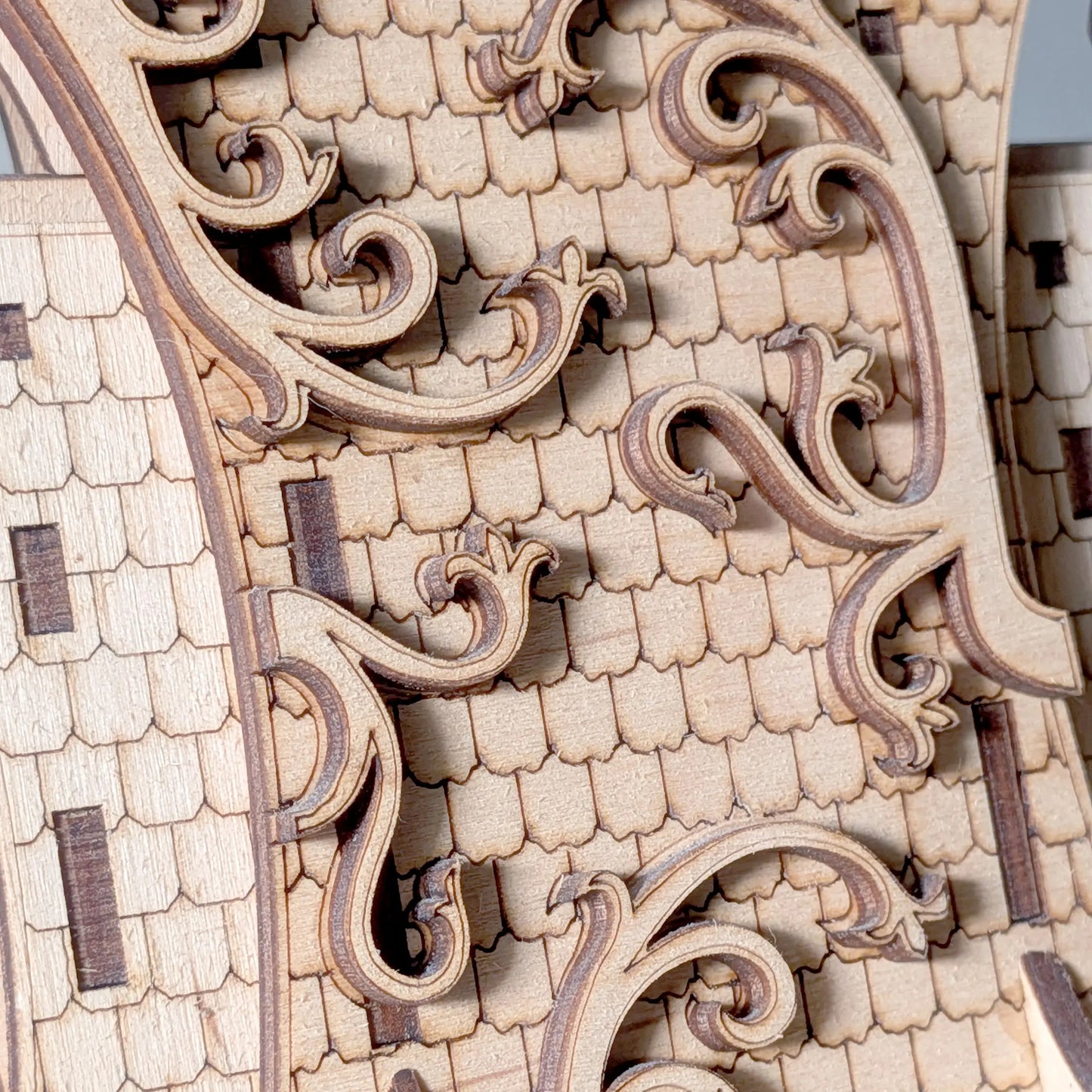 Macro texture shot of an intricate shingle roof with swirling filigree carved from natural laser cut plywood layers.