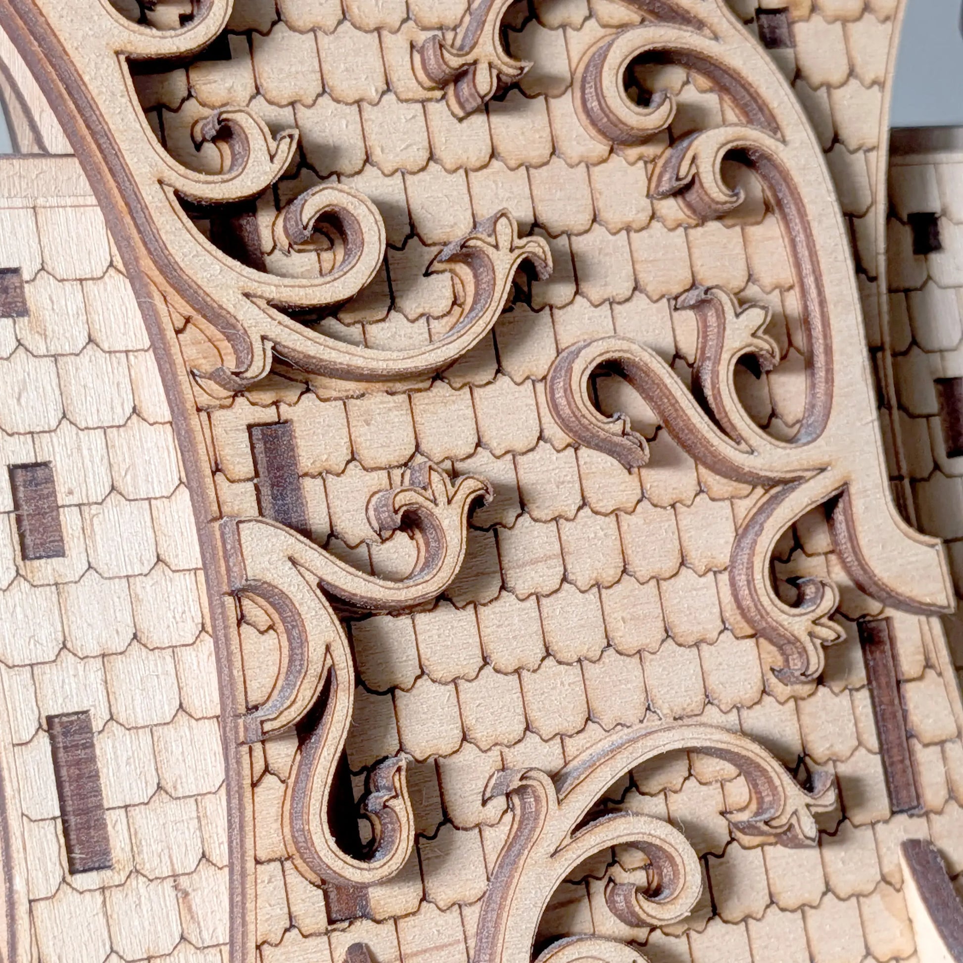 Macro texture shot of an intricate shingle roof with swirling filigree carved from natural laser cut plywood layers.