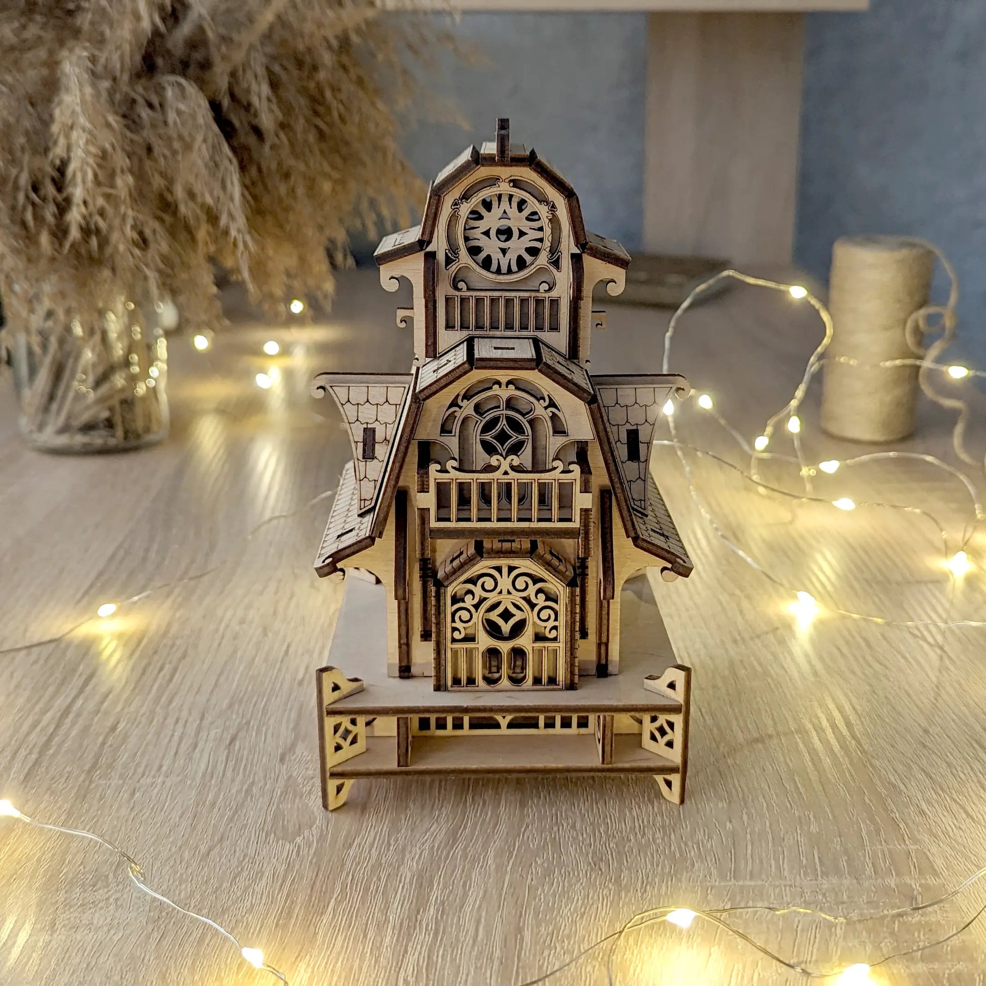 Symmetrical front view of the standalone laser cut plywood dollhouse puzzle resting near a spool of natural twine.