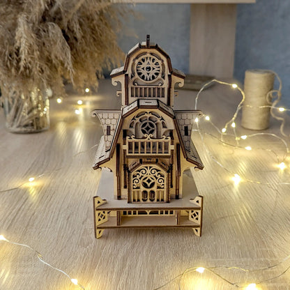 Symmetrical front view of the standalone laser cut plywood dollhouse puzzle resting near a spool of natural twine.