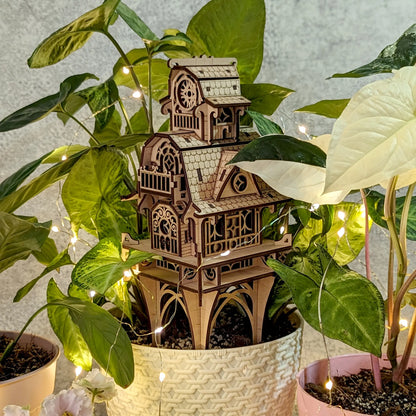 Elegant vertical presentation of the 3D laser cut plywood fairy castle structure, surrounded by green plant leaves.