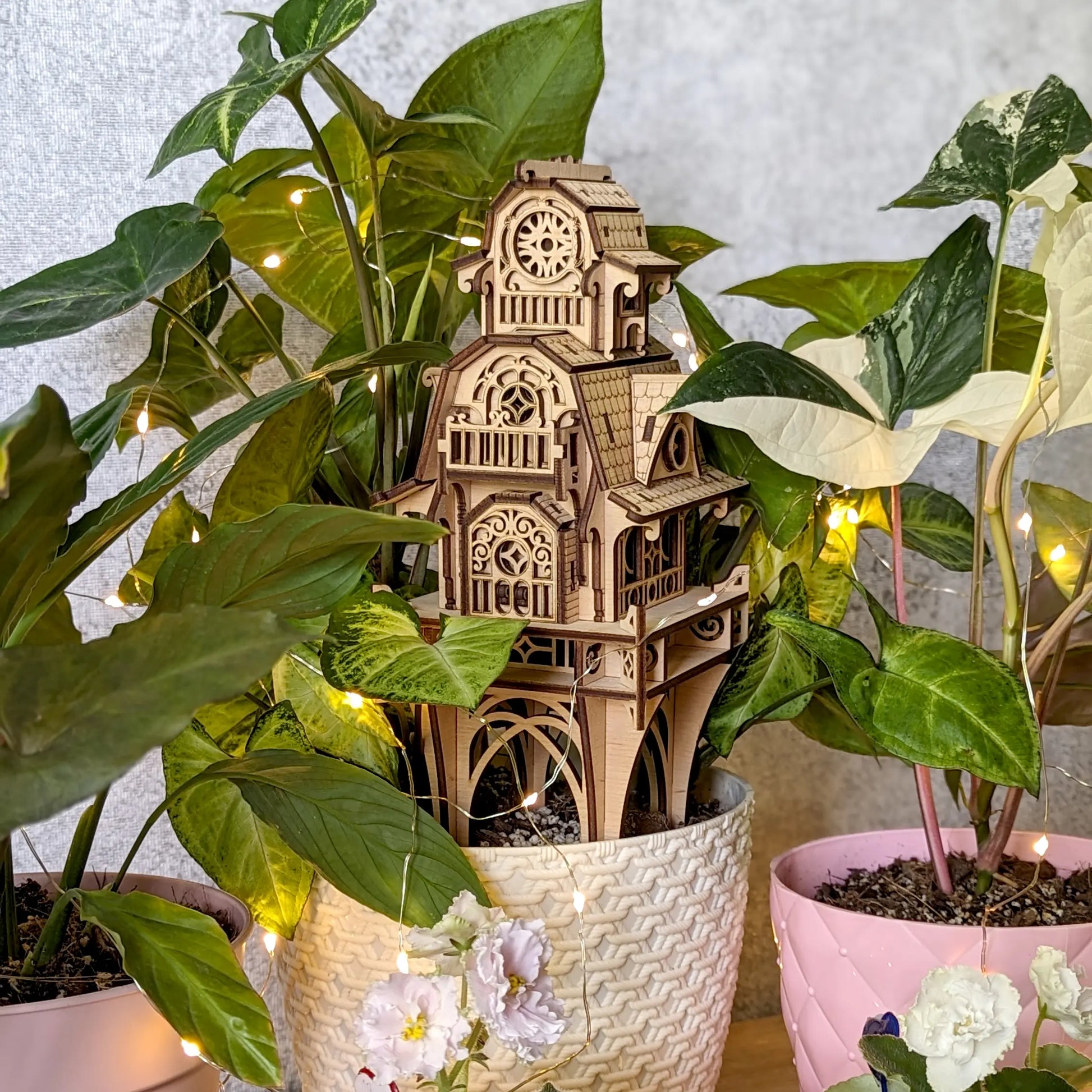 Vertical close-up of the laser cut plywood ornamental garden stake house nestled into lush green indoor foliage.