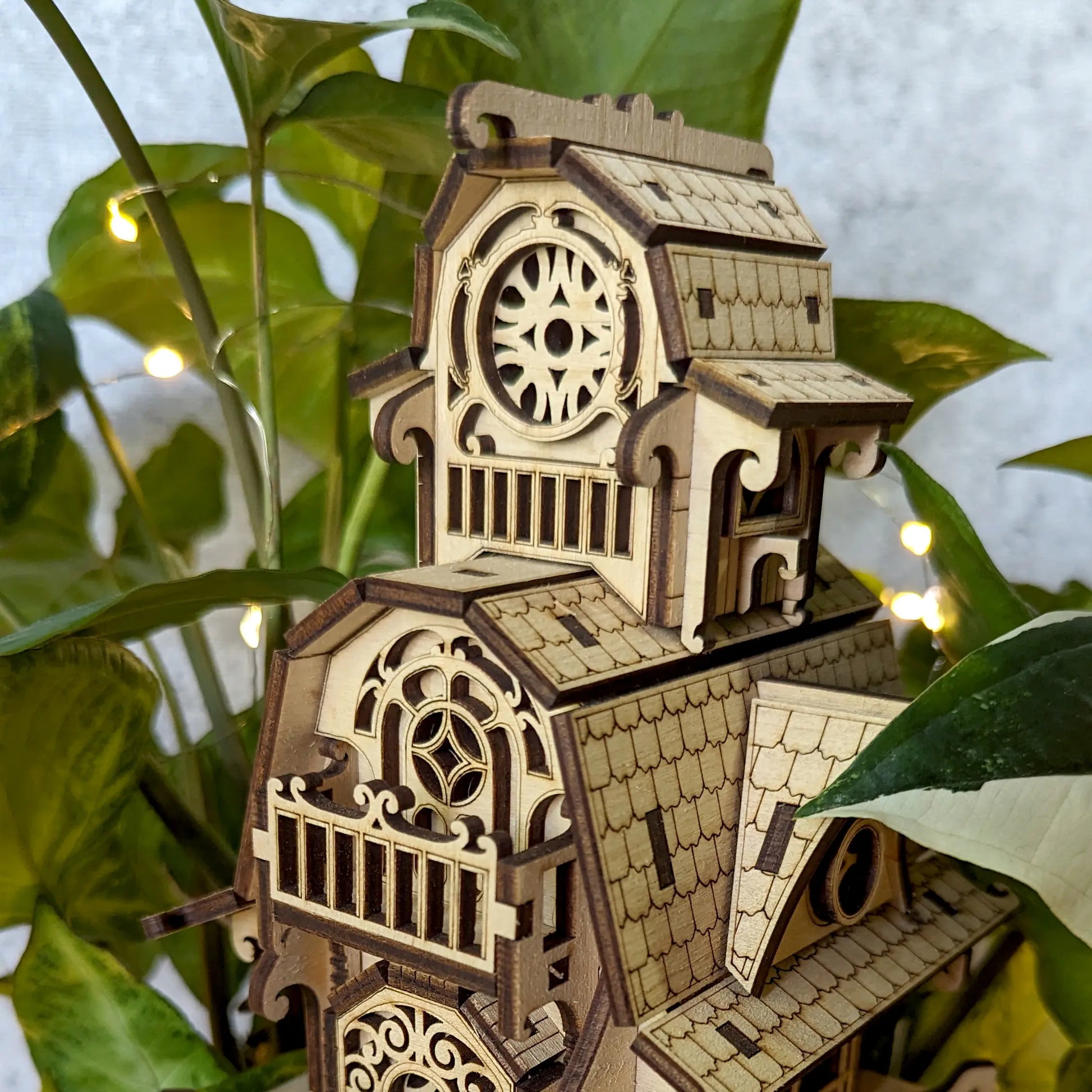 Close-up view of the upper levels of a laser cut plywood miniature home, showing a balcony and rose window details.