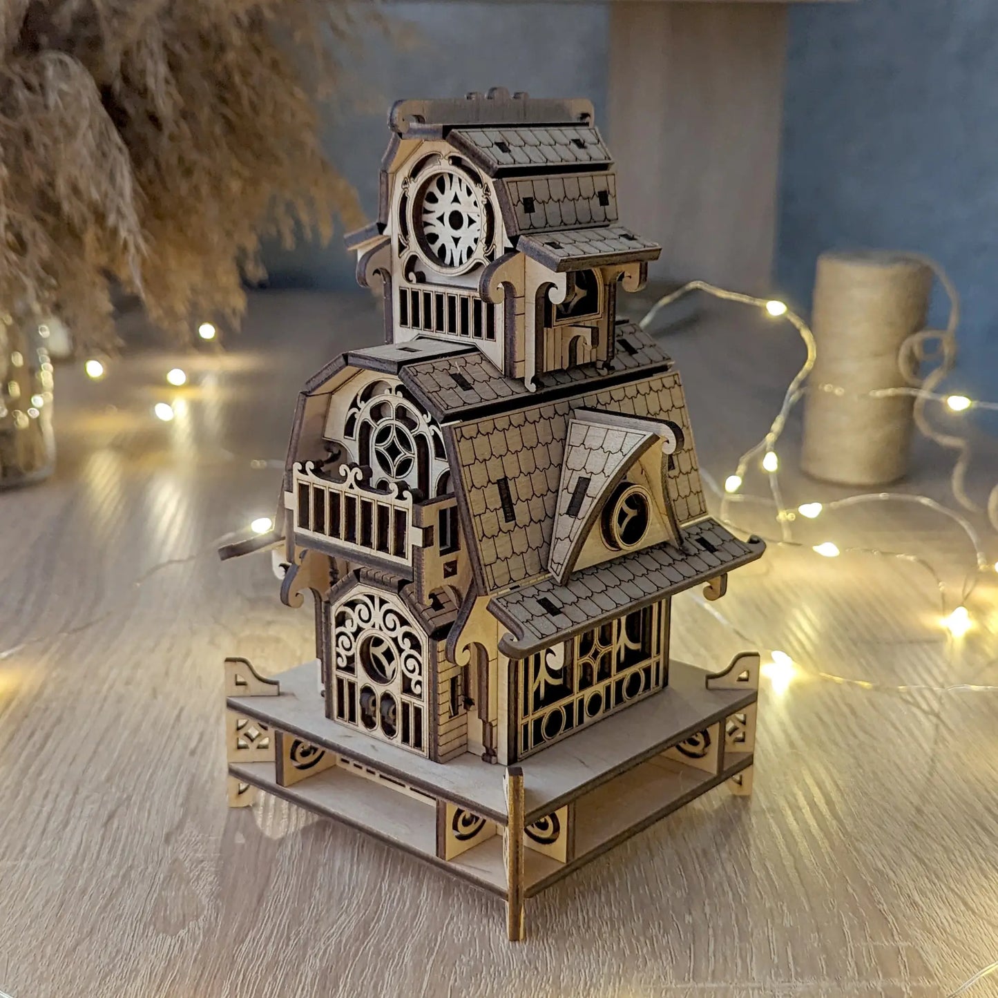 High-angle shot of the assembled laser cut plywood wizard cabin model on a table, decorated with bright fairy lights.