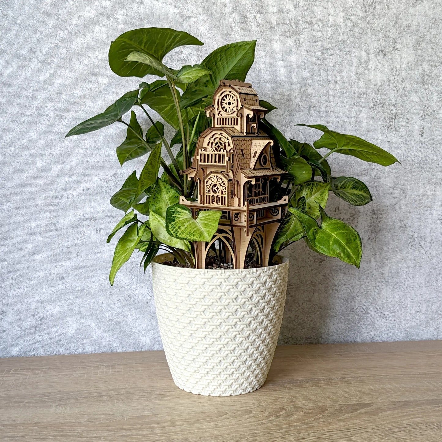 Eye-level studio photo of a laser cut plywood fantasy house stake standing tall inside a white textured flowerpot.