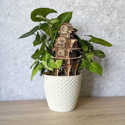 Eye-level studio photo of a laser cut plywood fantasy house stake standing tall inside a white textured flowerpot.