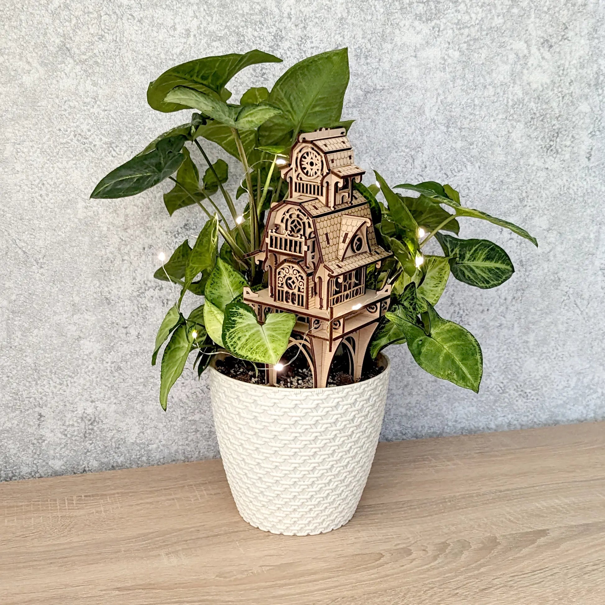 Wide horizontal view of a laser cut plywood enchanted castle stake staged inside a potted green plant with warm lights.