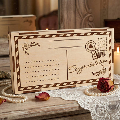 Laser cut plywood gift envelope designed like a postcard with "Congratulations" engraved in script. Features a striped border, stamp detail, and flower motifs. Displayed on a lace runner with pearls and a red rose for a romantic gift setting.