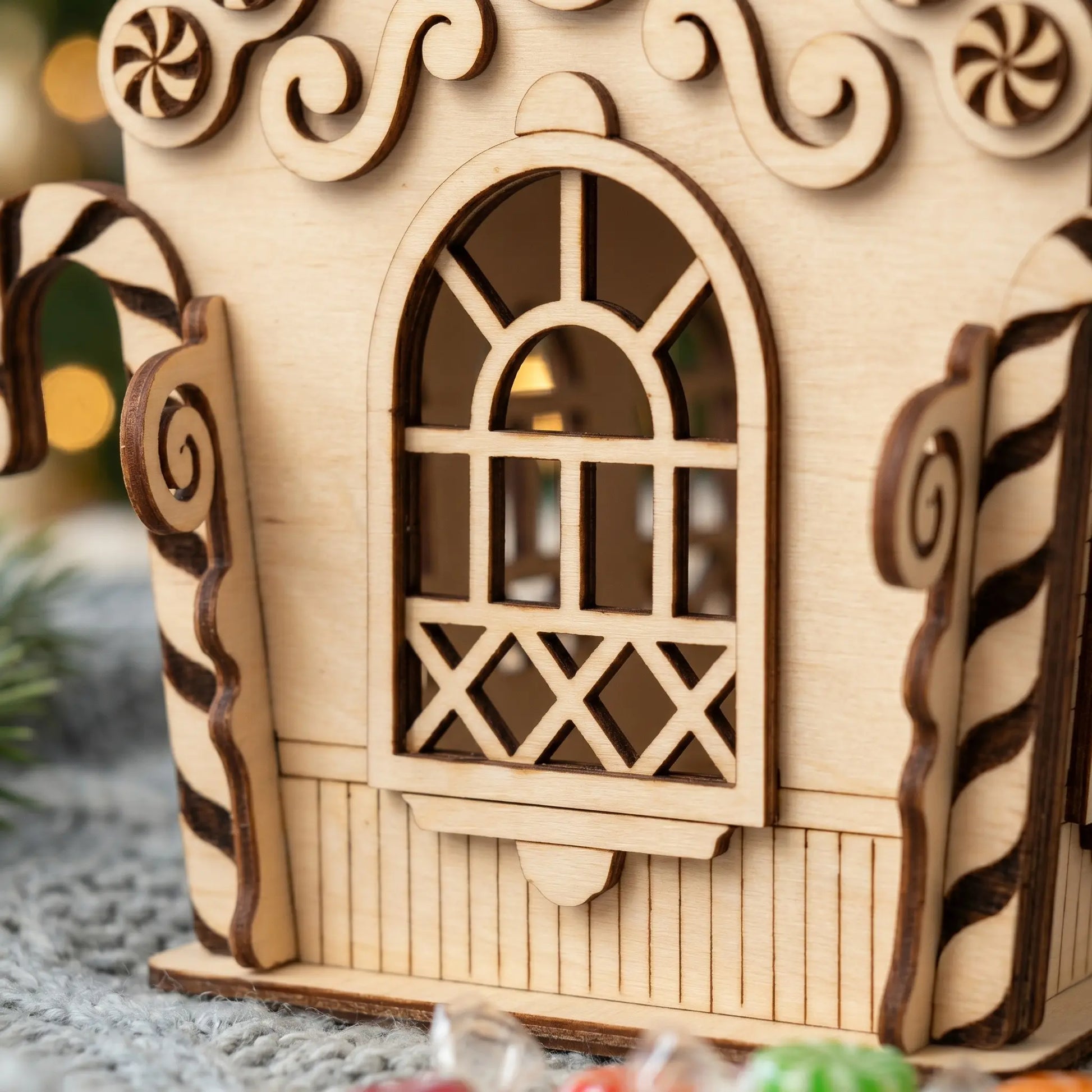 Wooden gingerbread house model with decorative elements on a soft surface.