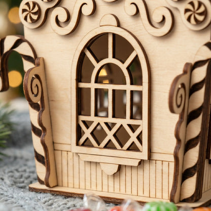 Wooden gingerbread house model with decorative elements on a soft surface.