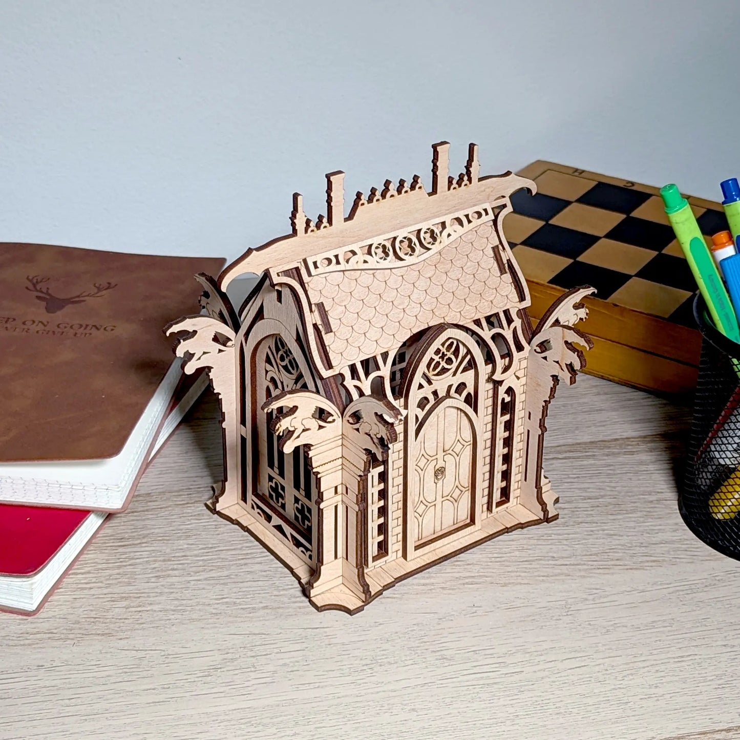 An assembled miniature gothic box styled on a wooden workspace next to a leather notebook, made of fine laser cut plywood.
