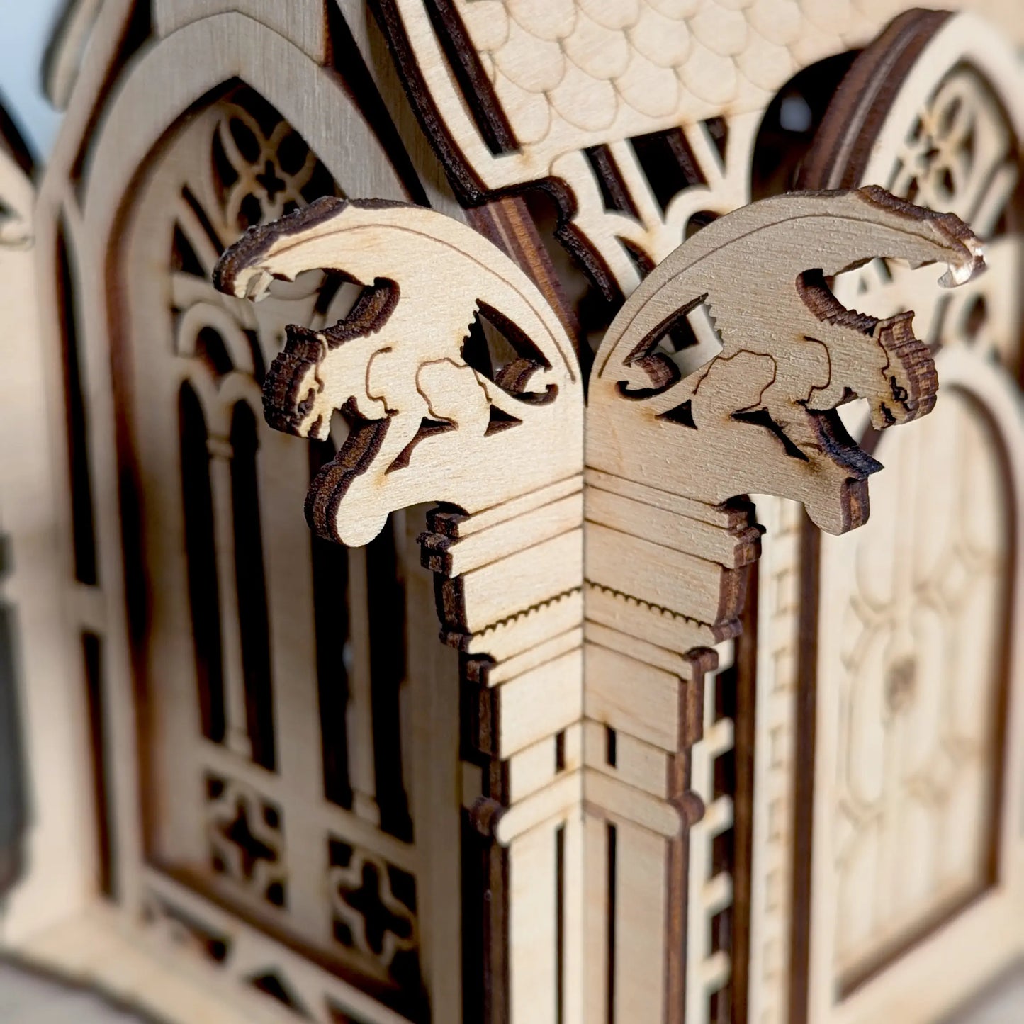A detailed macro photo focusing on the two tiny engraved gargoyles on a corner pillar made of layered laser cut plywood.