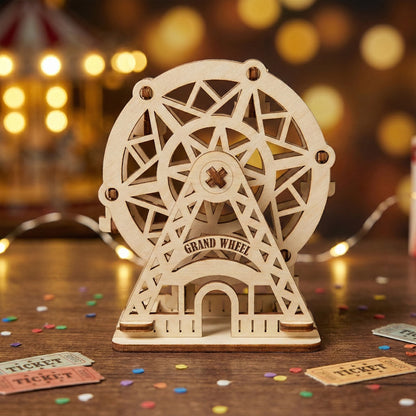 Front view of a decorative "Grand Wheel" Ferris wheel made of laser cut plywood. Features intricate geometric cutouts and a stable triangular base. Resting on a dark wood surface with festive tickets and blurred lights in the background.