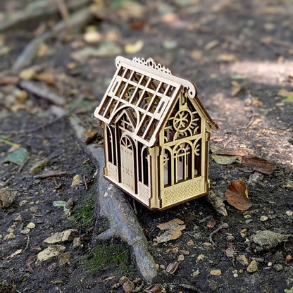 A straight eye-level front view of a decorative miniature tabletop greenhouse display made from layered laser cut plywood.