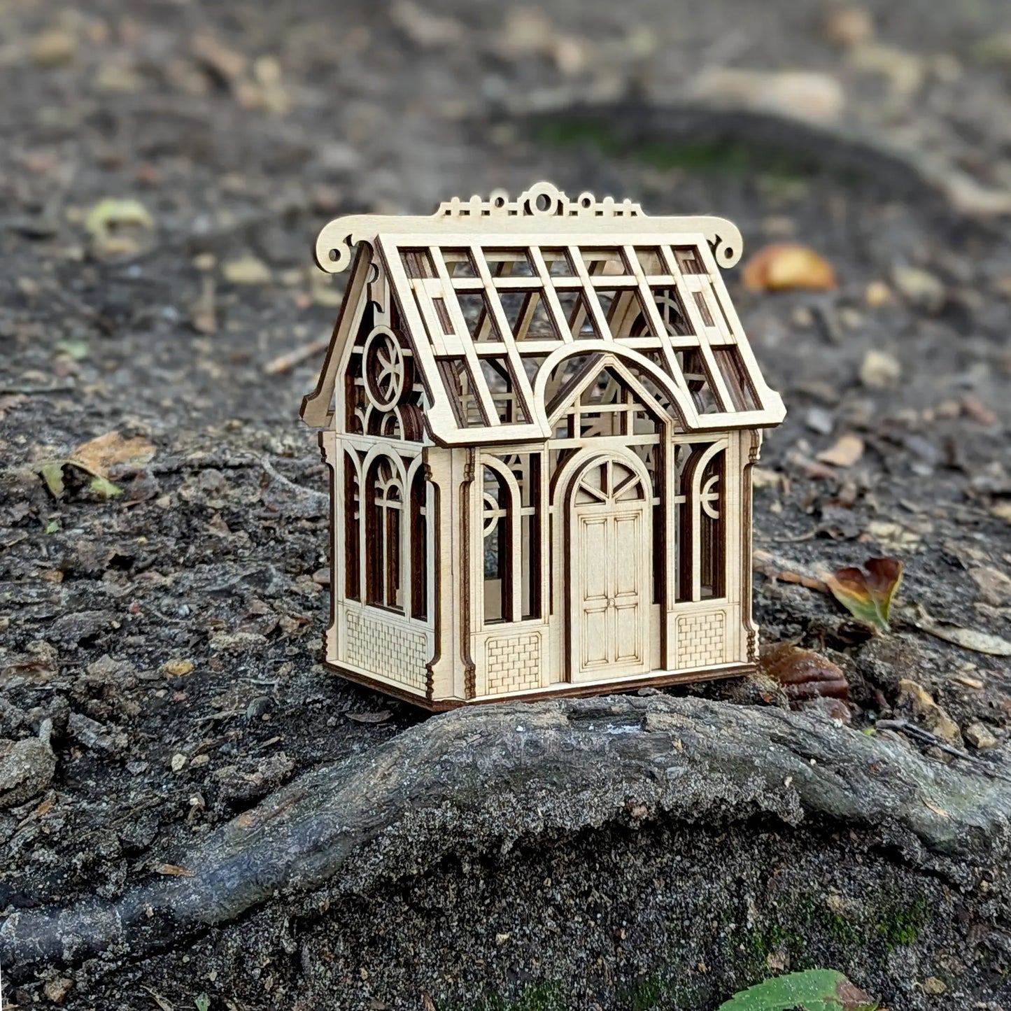 A beautiful macro close-up shot highlighting the delicate window frame details on a laser cut plywood miniature greenhouse.