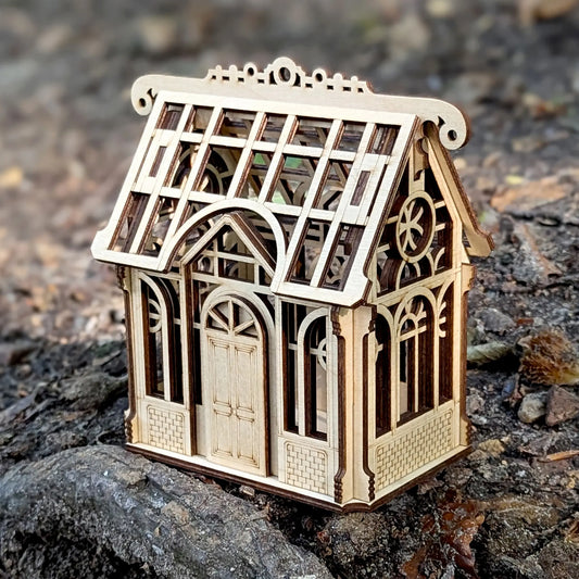 Three-quarter view of an assembled miniature house greenhouse puzzle made from fine laser cut plywood.