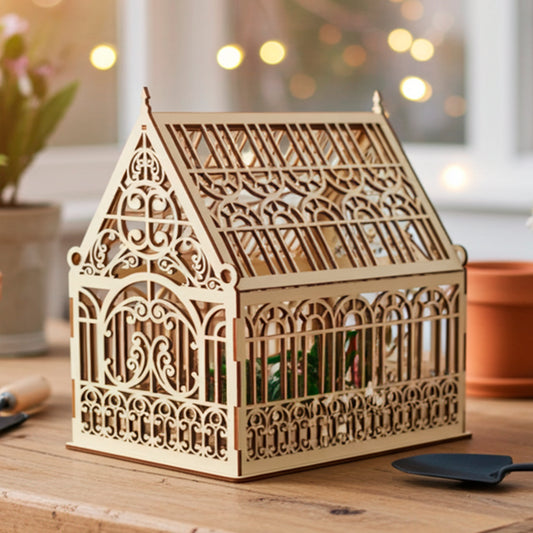 A laser-cut plywood wooden greenhouse model with intricate decorative panels and an openwork roof, shown from an angled view to highlight its detailed craftsmanship and light natural wood texture.