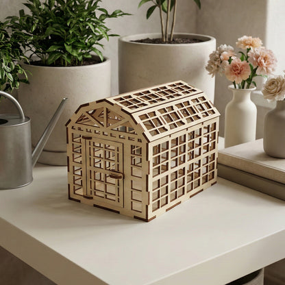 Wooden laser cut greenhouse model with open lattice walls, sloped roof, and detailed door framing, displayed against a softly blurred indoor plant shelf background.