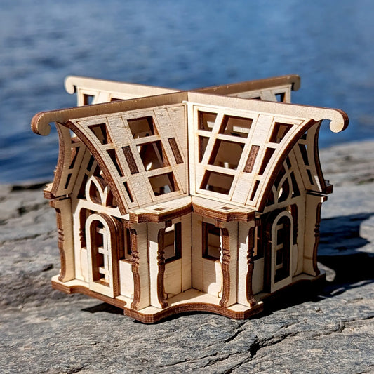 Laser cut plywood miniature orangery structure with geometric window panels on natural rock surface.