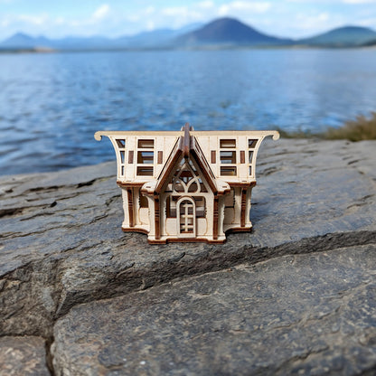 Straight front view of an intricate laser cut plywood glasshouse puzzle staged on rocks with a scenic lake and mountains.