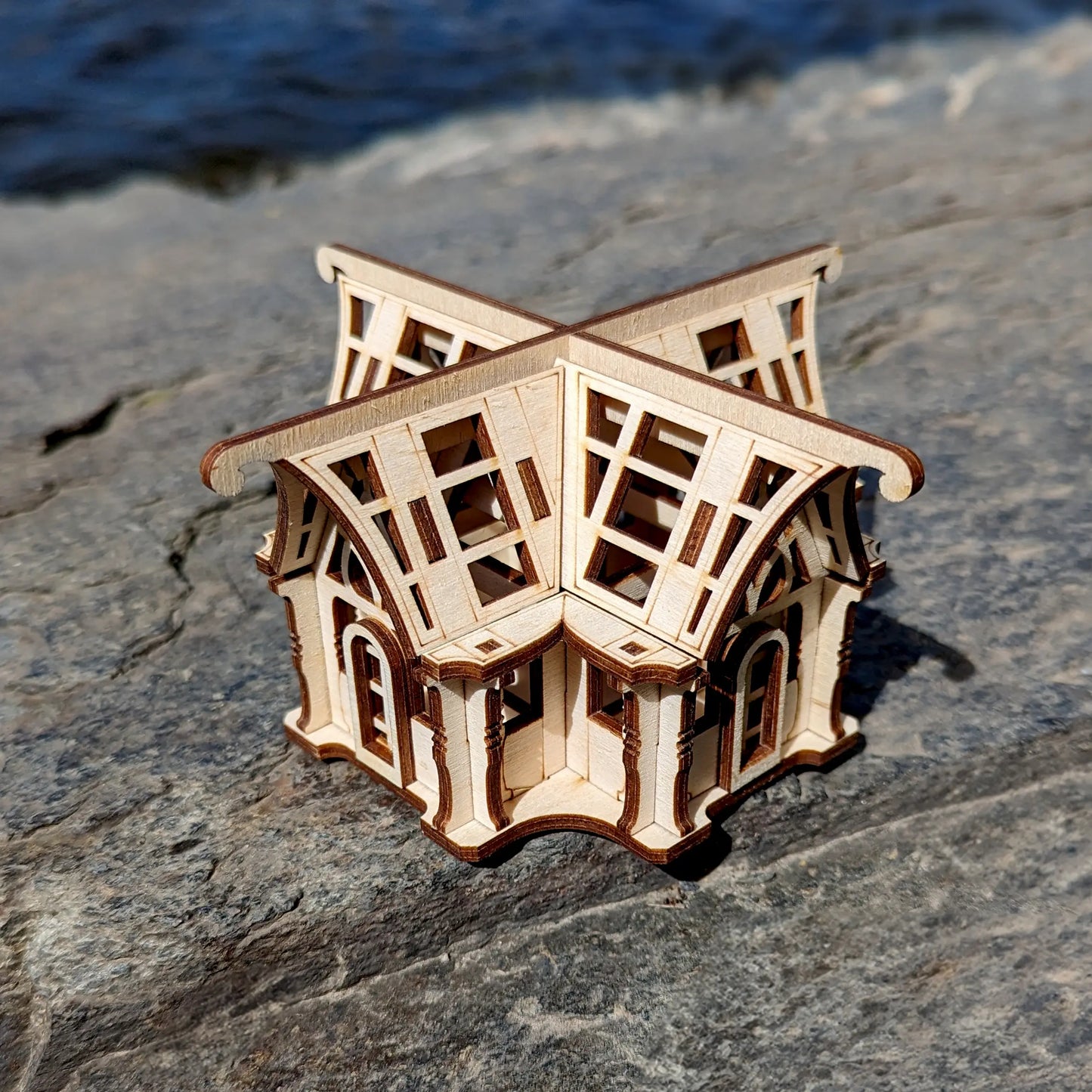 Perspective look of a laser cut plywood architectural scale model greenhouse sitting outdoors on textured granite block.