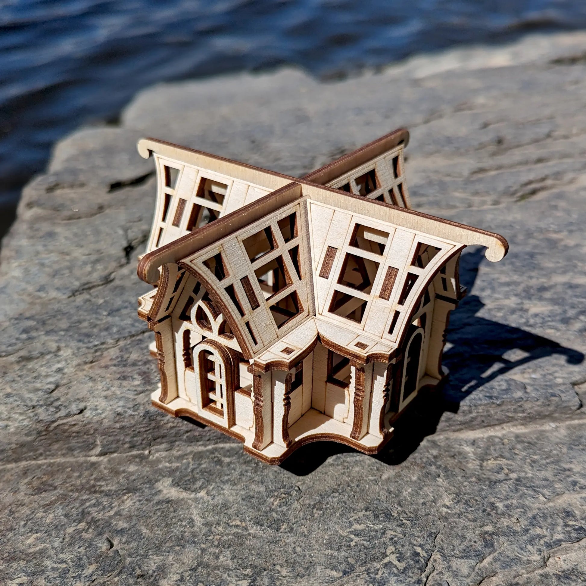 Back side perspective view of a mini traditional glasshouse cottage prototype constructed out of laser cut plywood rows.