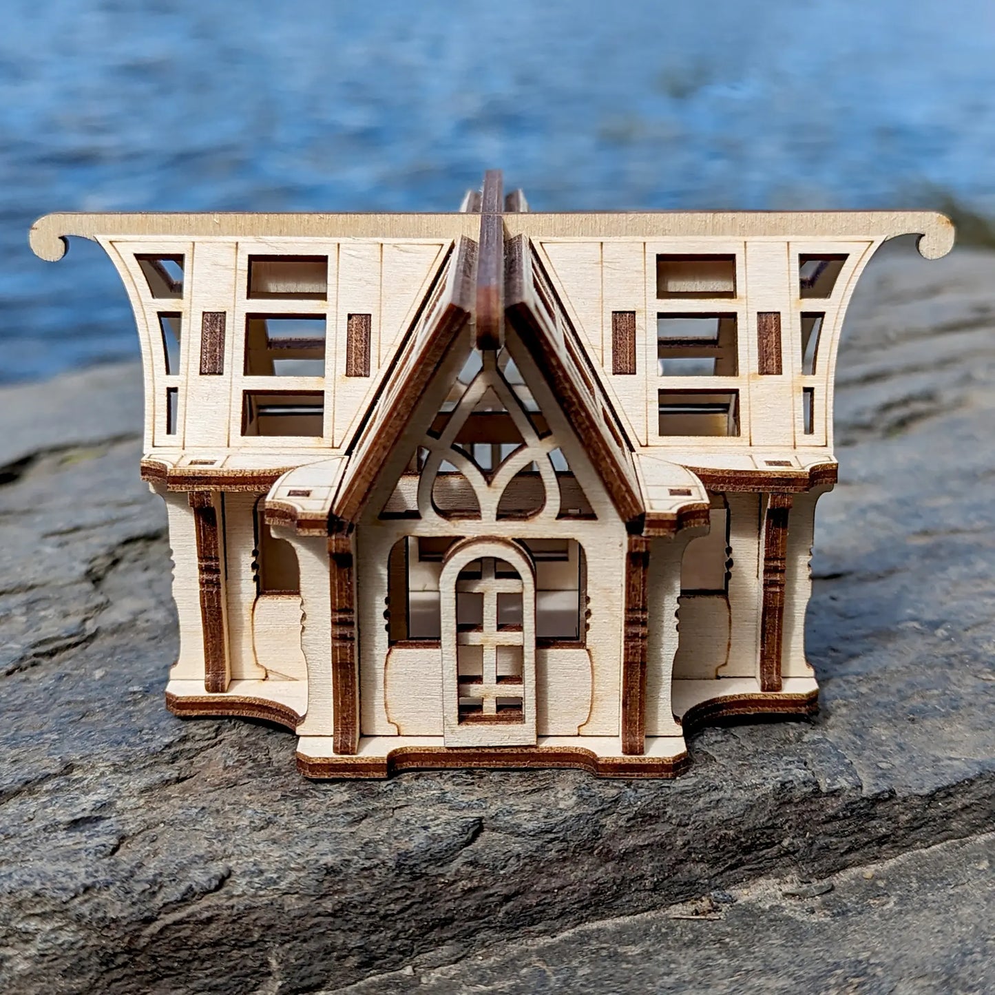 Front-facing macro view of a 3D laser cut plywood orangery centerpiece model placed on a dark sunlit coastal stone rock.