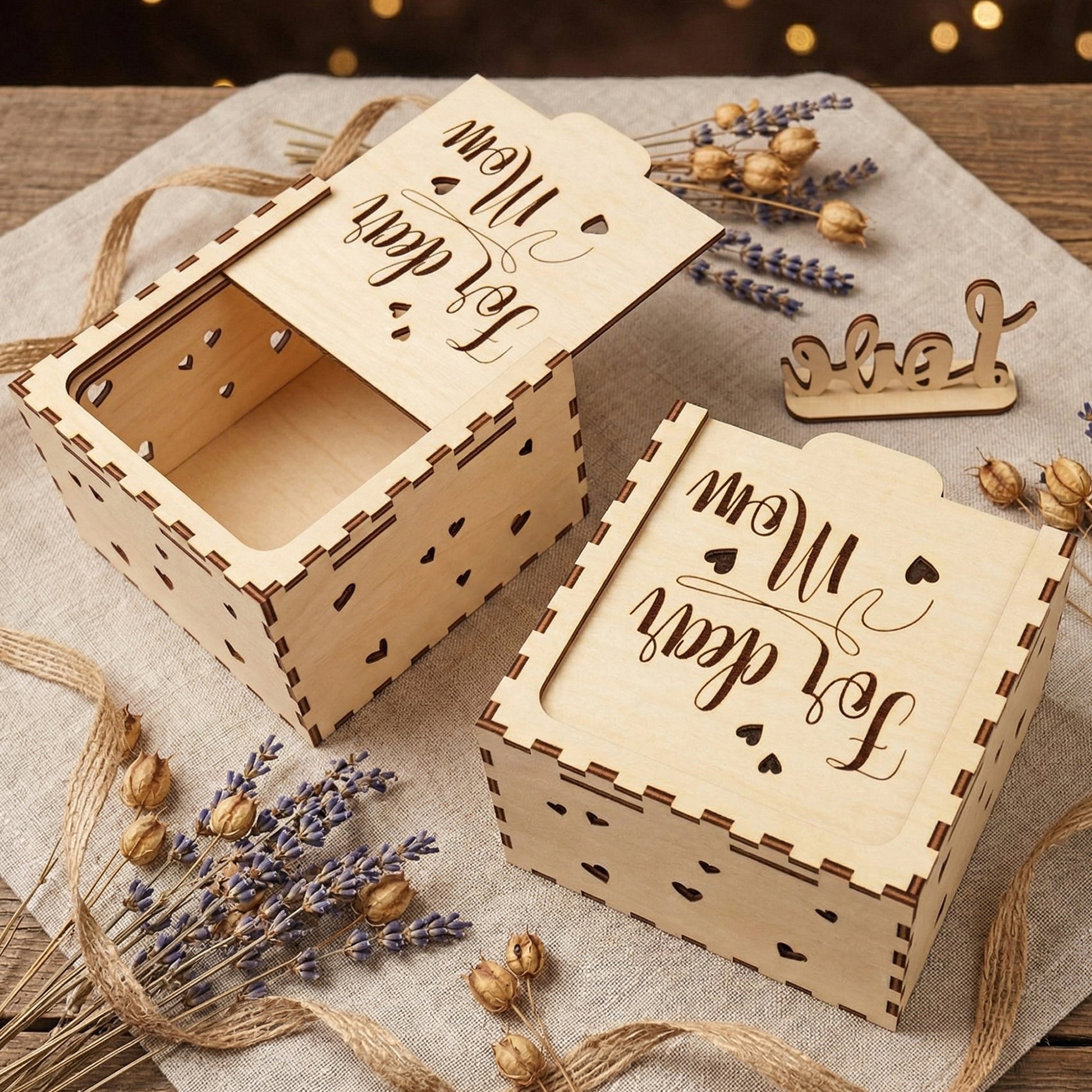 An angled top view of two "For dear Mom" laser-cut wooden boxes—one open and one closed. The high-quality plywood construction shows dark burnt edges and heart-shaped side details. Arranged with rustic twine and dried lavender, perfect for Mother’s Day or a personalized birthday gift presentation.