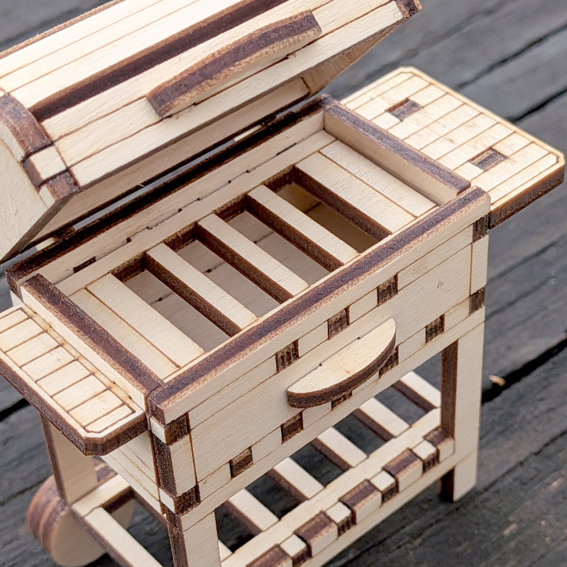 Close-up view of the laser cut wooden BBQ grill top, showing the open lid and slatted grill area with detailed wood joinery.