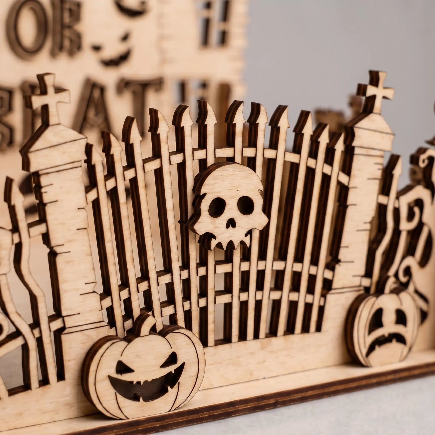 Wooden Halloween decoration with a skull design on a fence, pumpkins, and blurred text in the background.