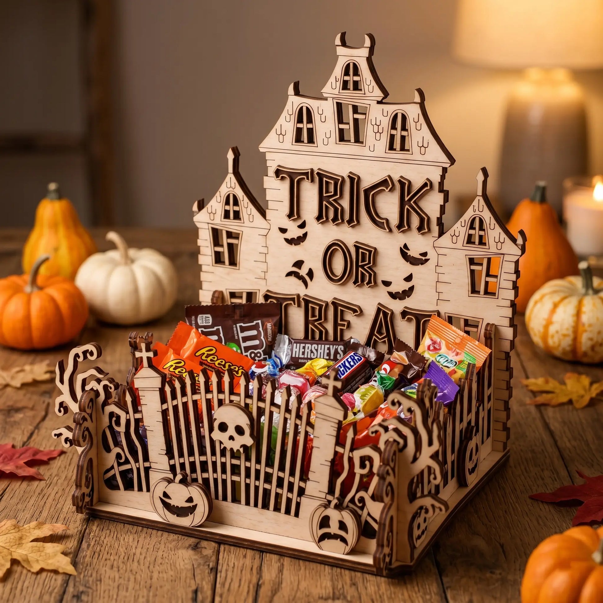Wooden laser cut Halloween candy holder with treats on a wooden table with pumpkins.