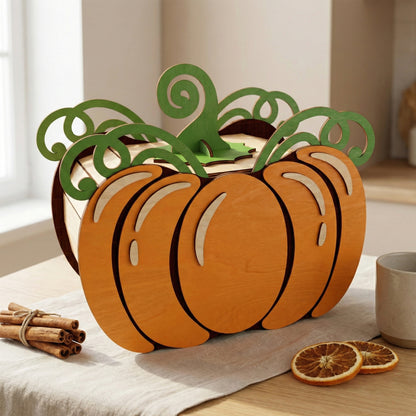Front view of a pumpkin-shaped storage box made of laser cut plywood. Features orange-stained outer layers and green vine-like accents on top. The wooden box sits on a linen cloth next to cinnamon sticks and dried orange slices for a cozy fall vibe.