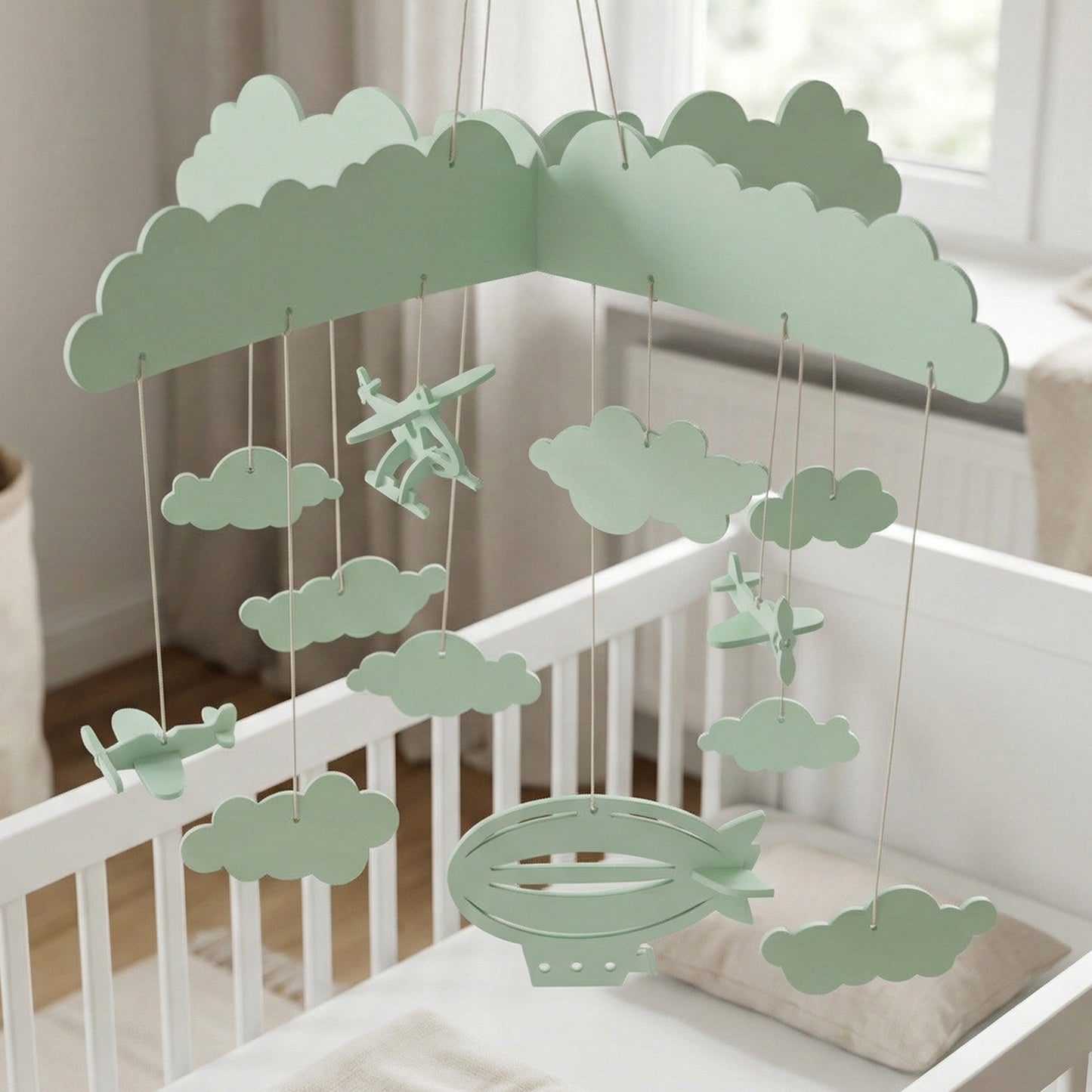 Mint green laser cut wooden hanging toy composed of fluffy clouds, small airplanes, and a blimp, intended as a baby crib mobile.