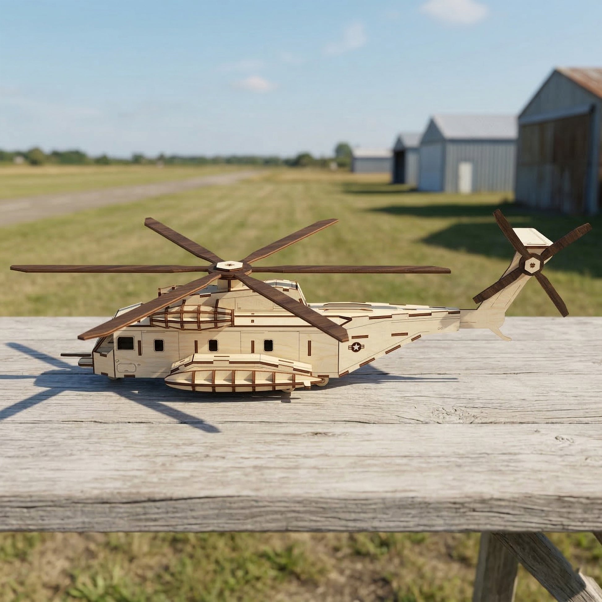 Side profile of a laser cut plywood helicopter aircraft model. Detailed fuselage features an etched military star insignia, tail rotor, and side sponsons. Crafted from light-colored wood, resting on a weathered table at an outdoor airfield.