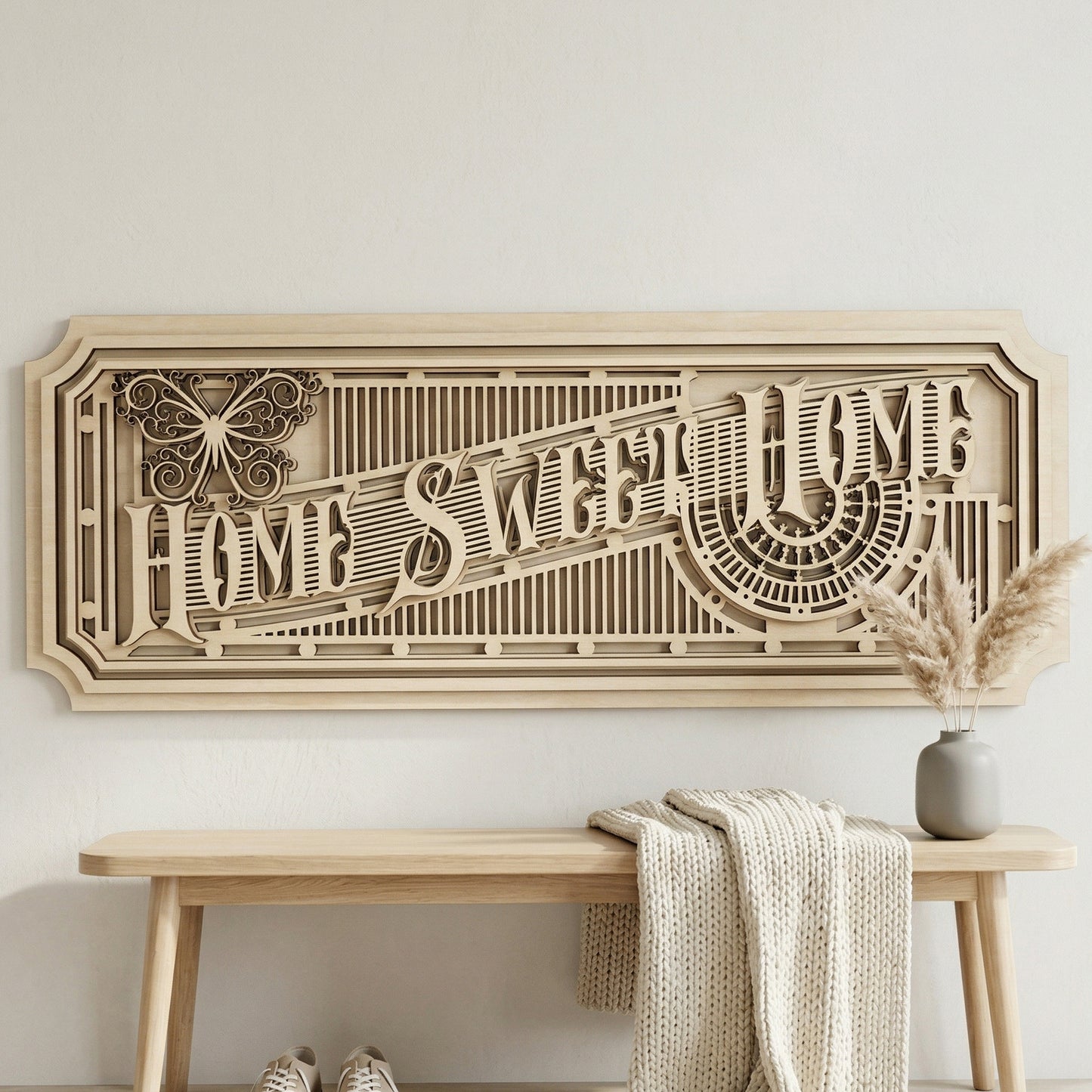 Frontal view of an architectural 3D "Home Sweet Home" wall art piece made from layered light-colored plywood. The horizontal sign showcases precise laser-cut details, including a stylized butterfly and sunburst patterns. Styled in a minimalist entryway above a light wood bench with a cozy knitted throw.