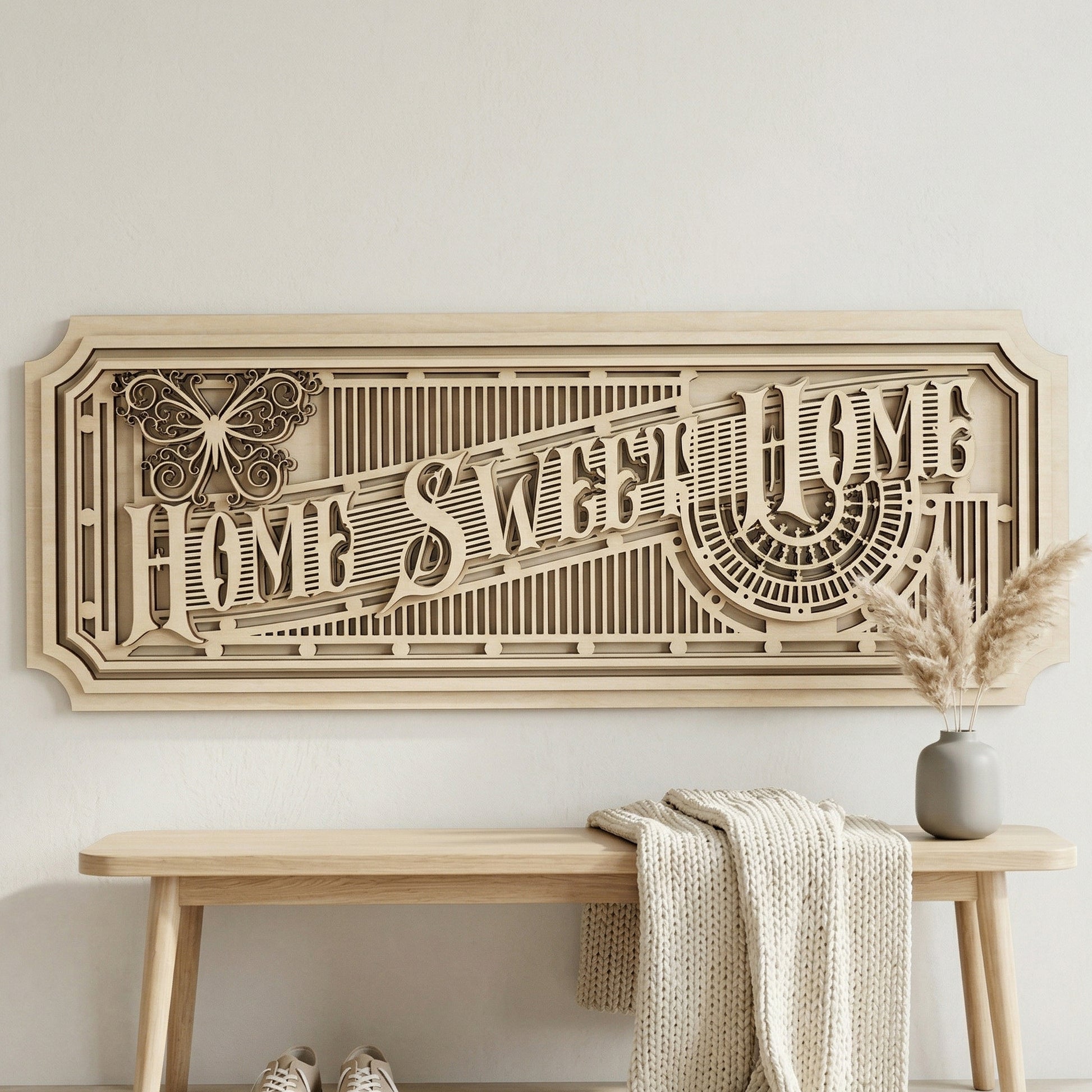 Frontal view of an architectural 3D "Home Sweet Home" wall art piece made from layered light-colored plywood. The horizontal sign showcases precise laser-cut details, including a stylized butterfly and sunburst patterns. Styled in a minimalist entryway above a light wood bench with a cozy knitted throw.