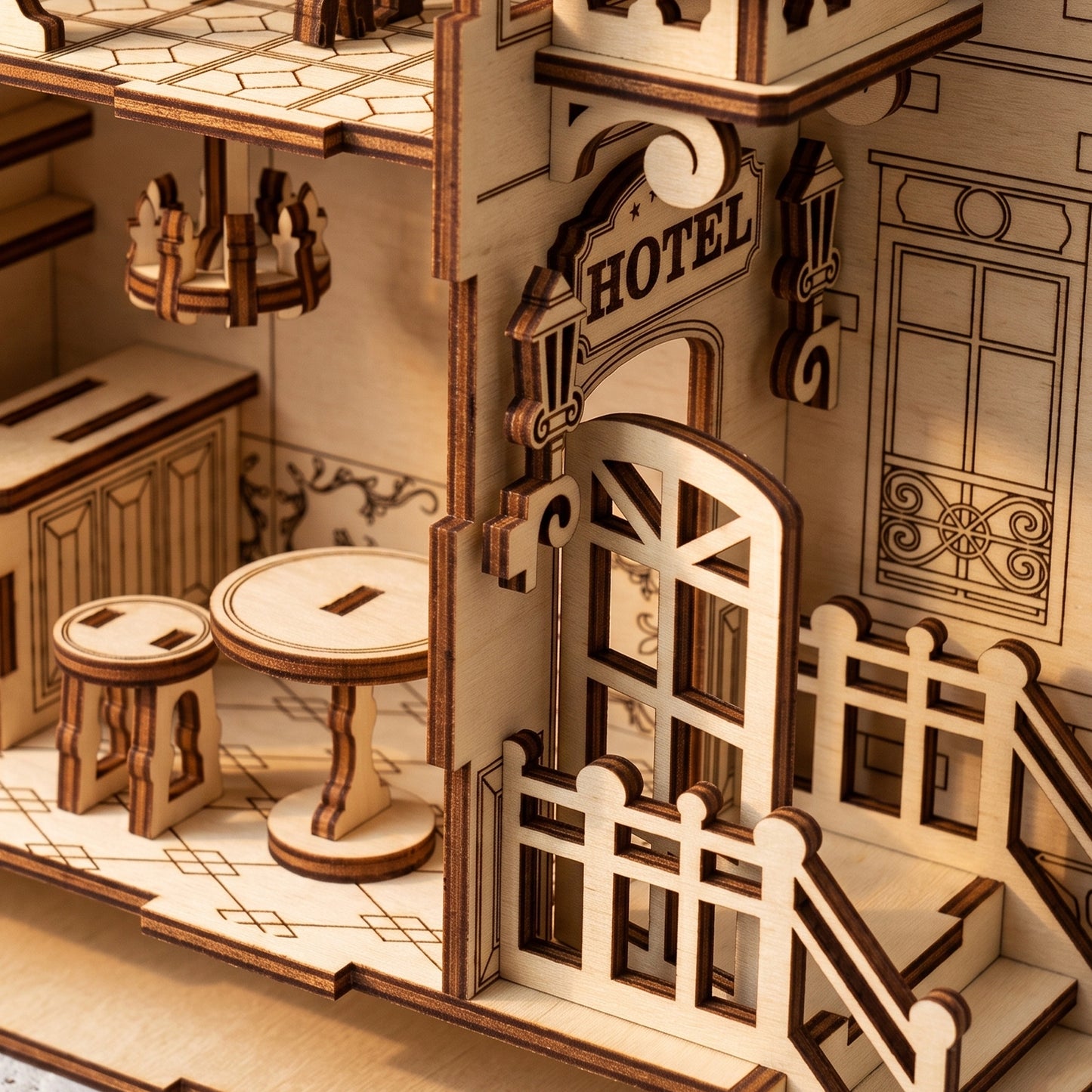 Close-up, top-down view of laser-cut birch plywood hotel book nook entrance with door, porch, and interior table. Dark burnt edges show fine wood grain.