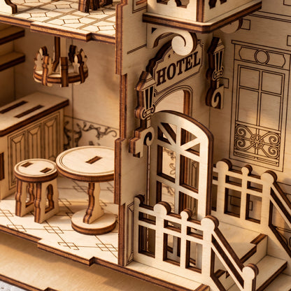 Close-up, top-down view of laser-cut birch plywood hotel book nook entrance with door, porch, and interior table. Dark burnt edges show fine wood grain.
