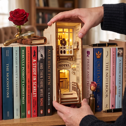Hands holding a laser-cut birch plywood hotel book nook. Warm lighting illuminates the detailed wooden interior, natural grain, and dark burnt edges.