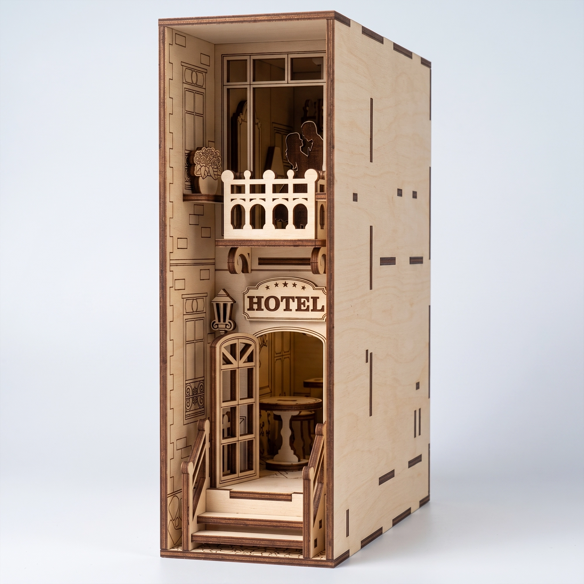 Three-quarter view of a light birch plywood laser-cut hotel book nook. Features a balcony with couple, entrance sign, and natural dark burnt edges.