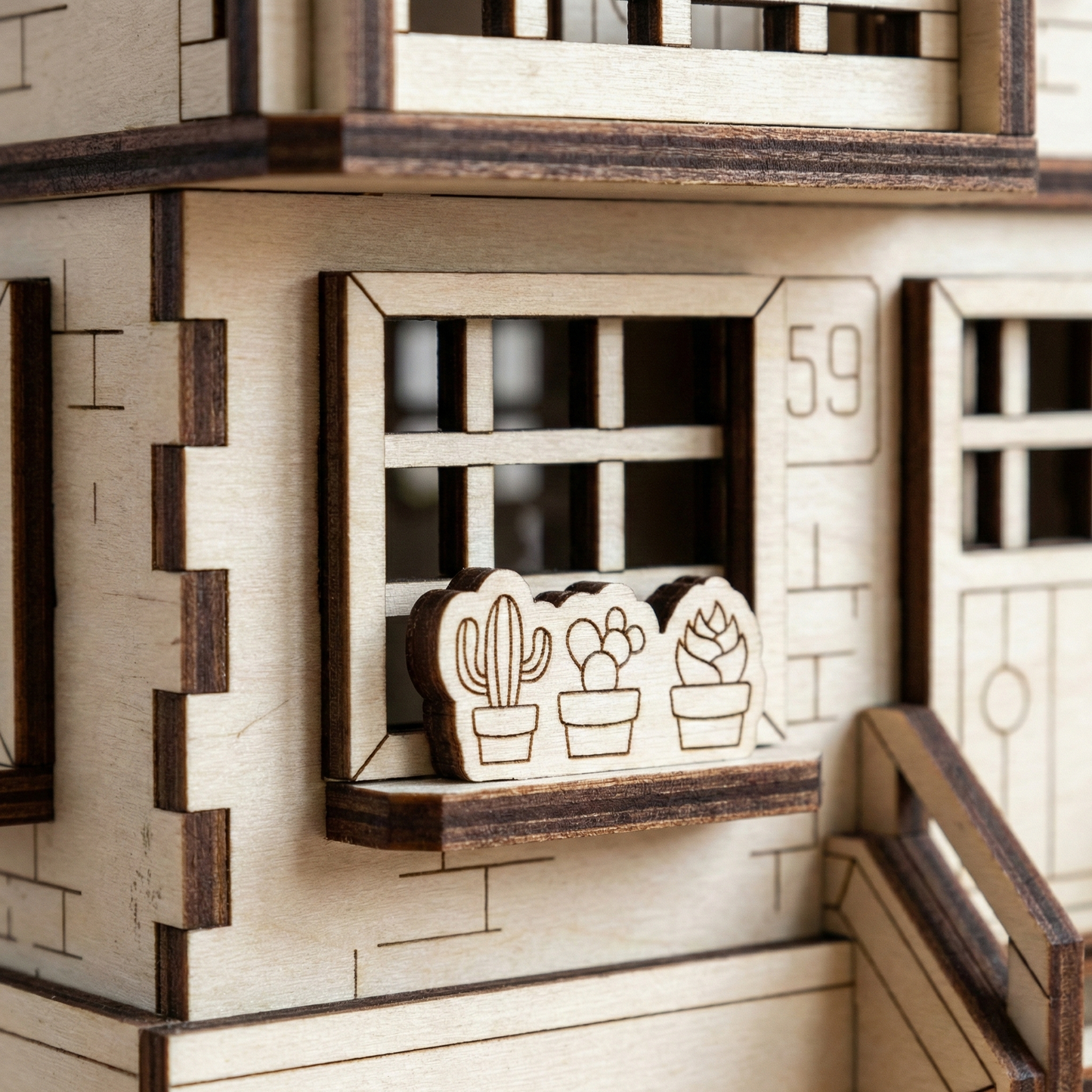 Wooden laser cut model of a house with a window displaying cactus decorations.