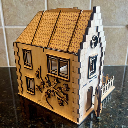 Side view of a laser cut plywood miniature house featuring an engraved blooming tree on the wall and an open front door.