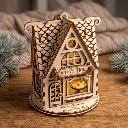 Glowing illuminated laser cut plywood Santa's House lantern on wood table with knit blanket and pine.