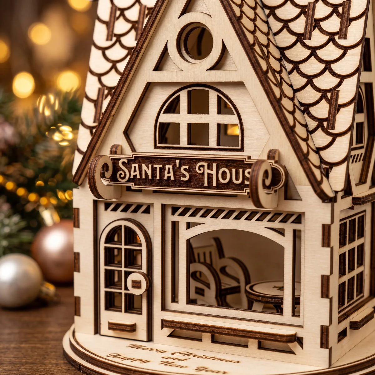 Close-up of laser cut plywood Santa's House sign and miniature interior furniture by holiday baubles.