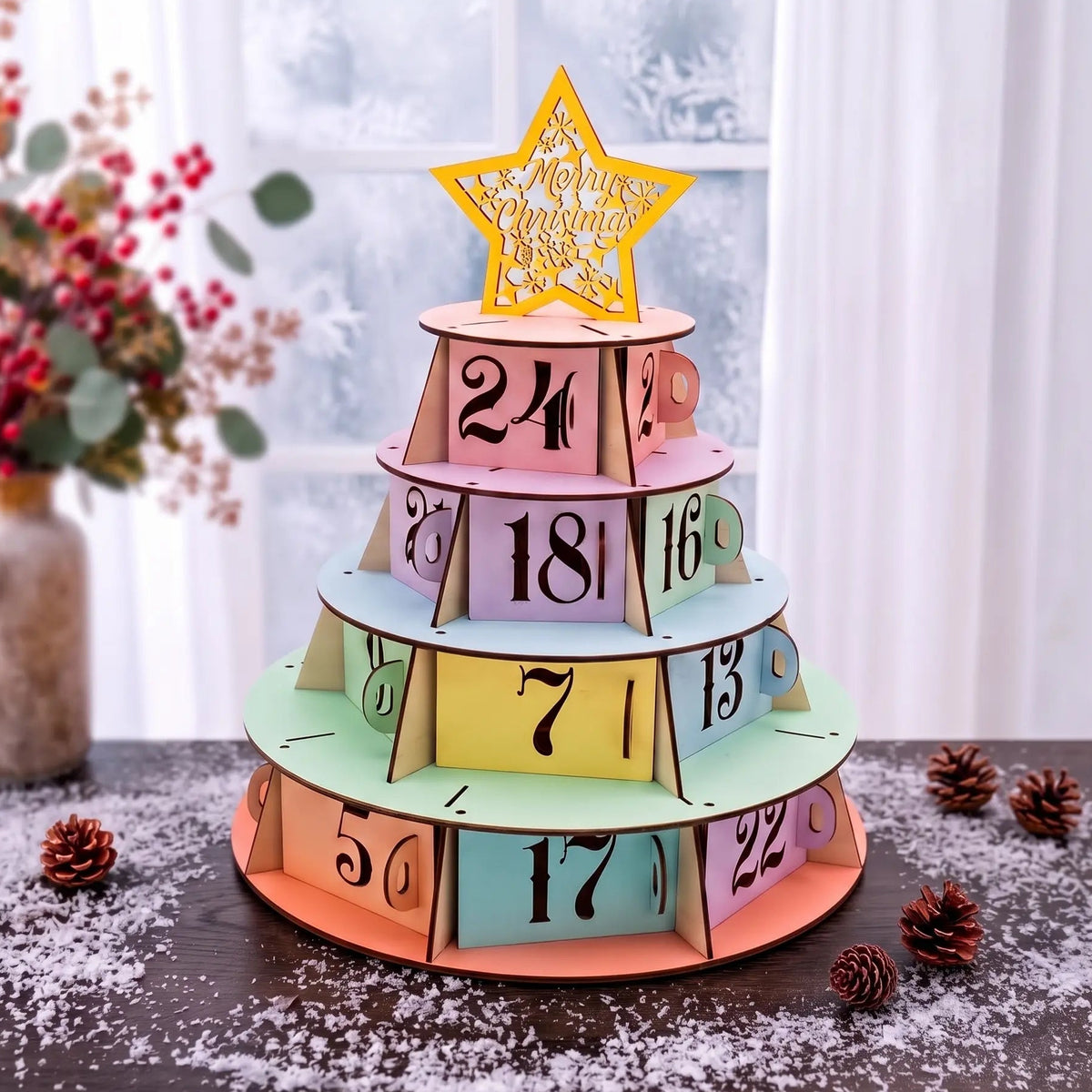 Pastel laser cut plywood Christmas tree advent calendar with star topper on snowy table near winter window and red berries.
