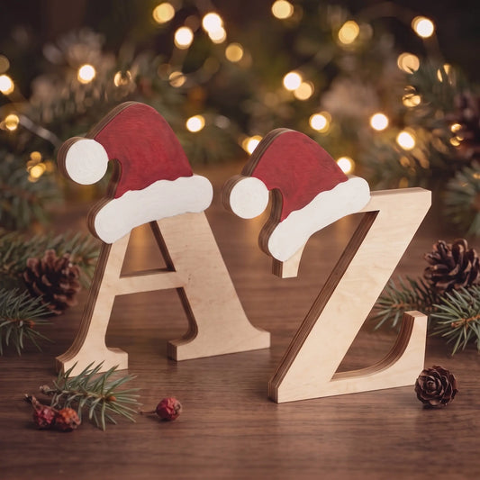Freestanding laser cut plywood letters A and Z with hand-painted Santa hats on wood table near warm fairy lights.