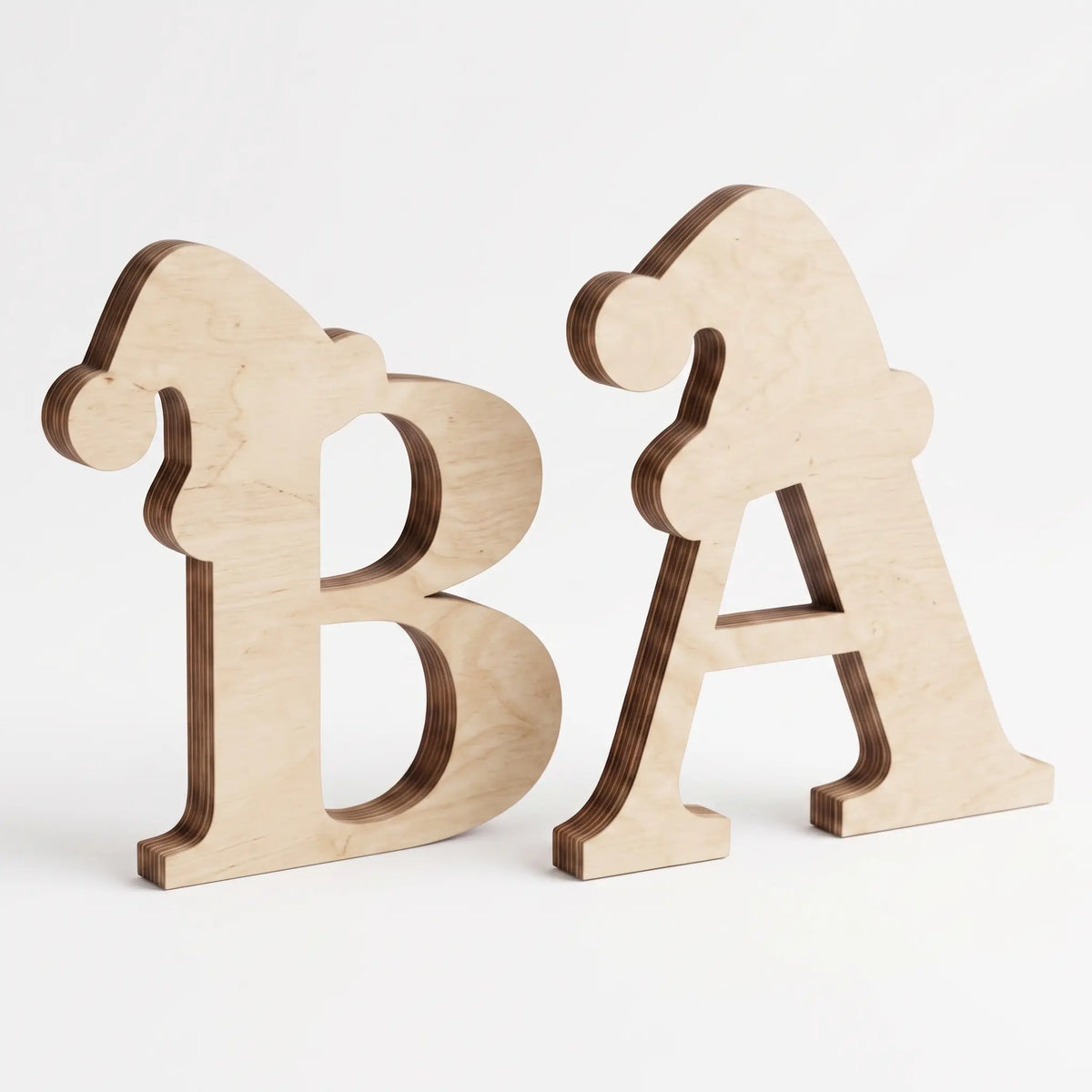 Side-angle view of unpainted laser cut plywood letters B and A wearing Santa hats, standing on plain white surface.