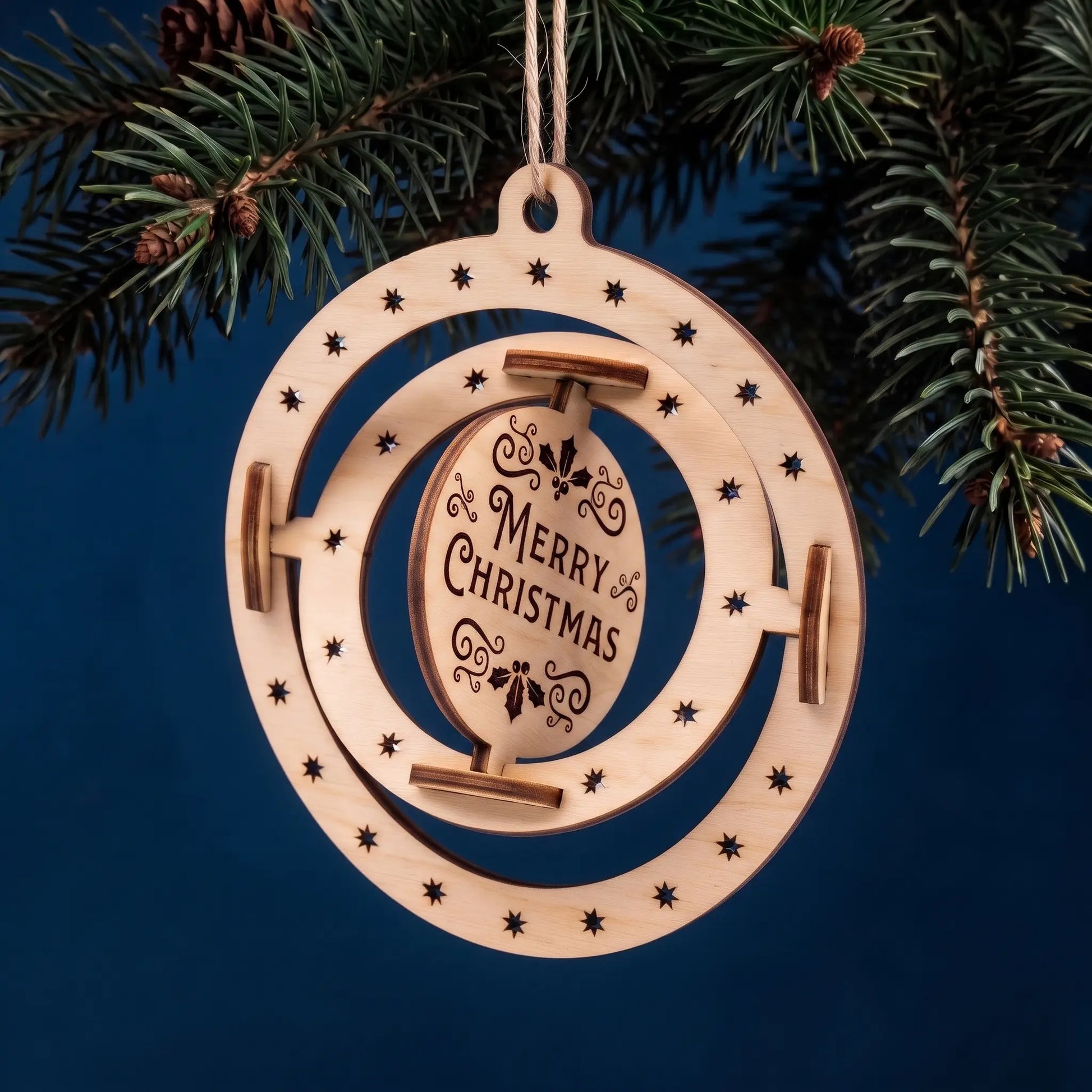 3D kinetic laser cut plywood sphere ornament with spinning Merry Christmas centerpiece hanging under fir needles.